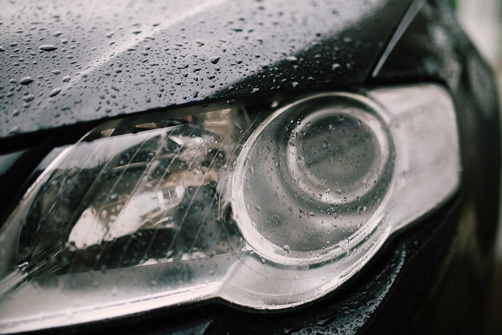 Close-up of a dark car's headlight and front fender covered in tight beads of water after a protective coating